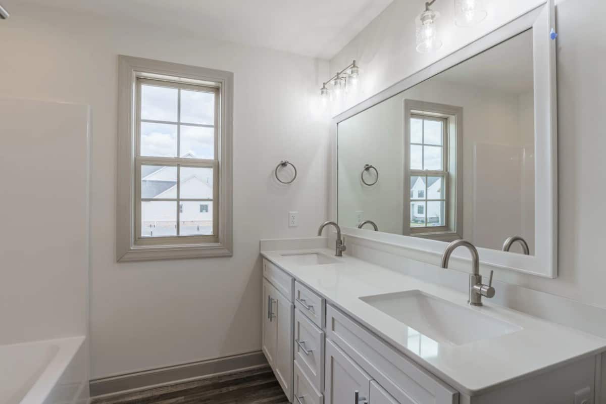 This bathroom offers a dual sink vanity topped with a rectangular mirror and glass sconces.
