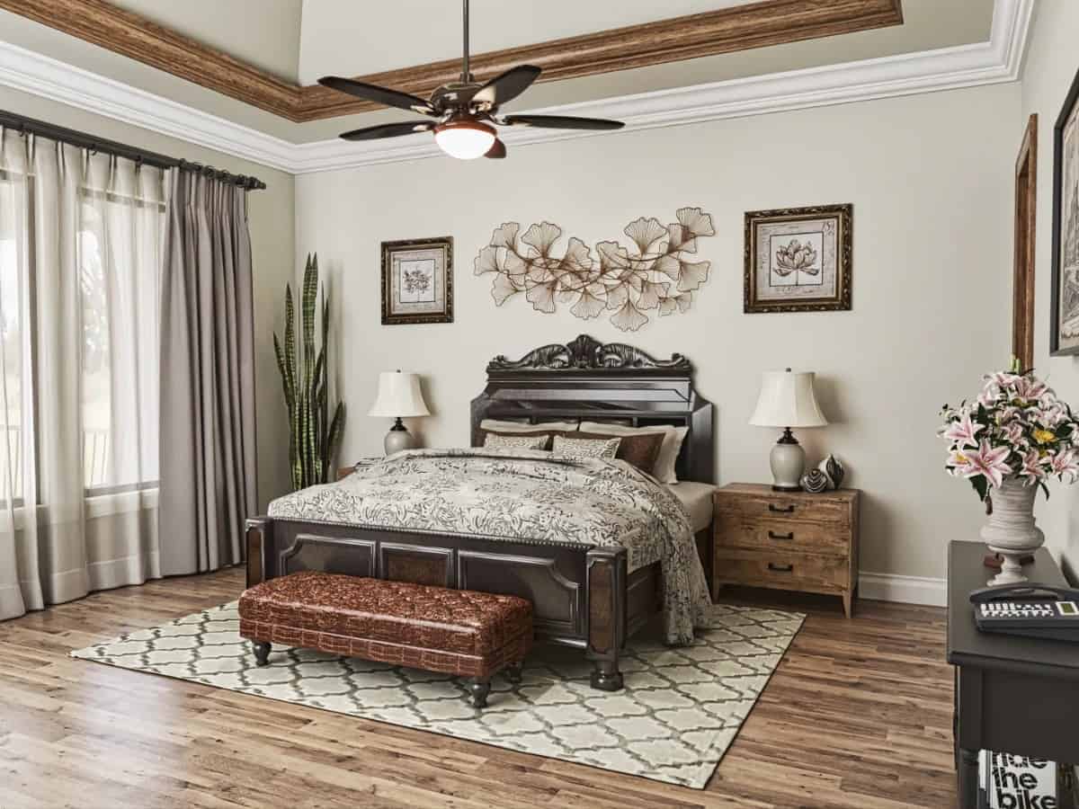 The primary bedroom features a coved ceiling, floral artworks, and an intricate dark wood bed complemented with a tufted bench.