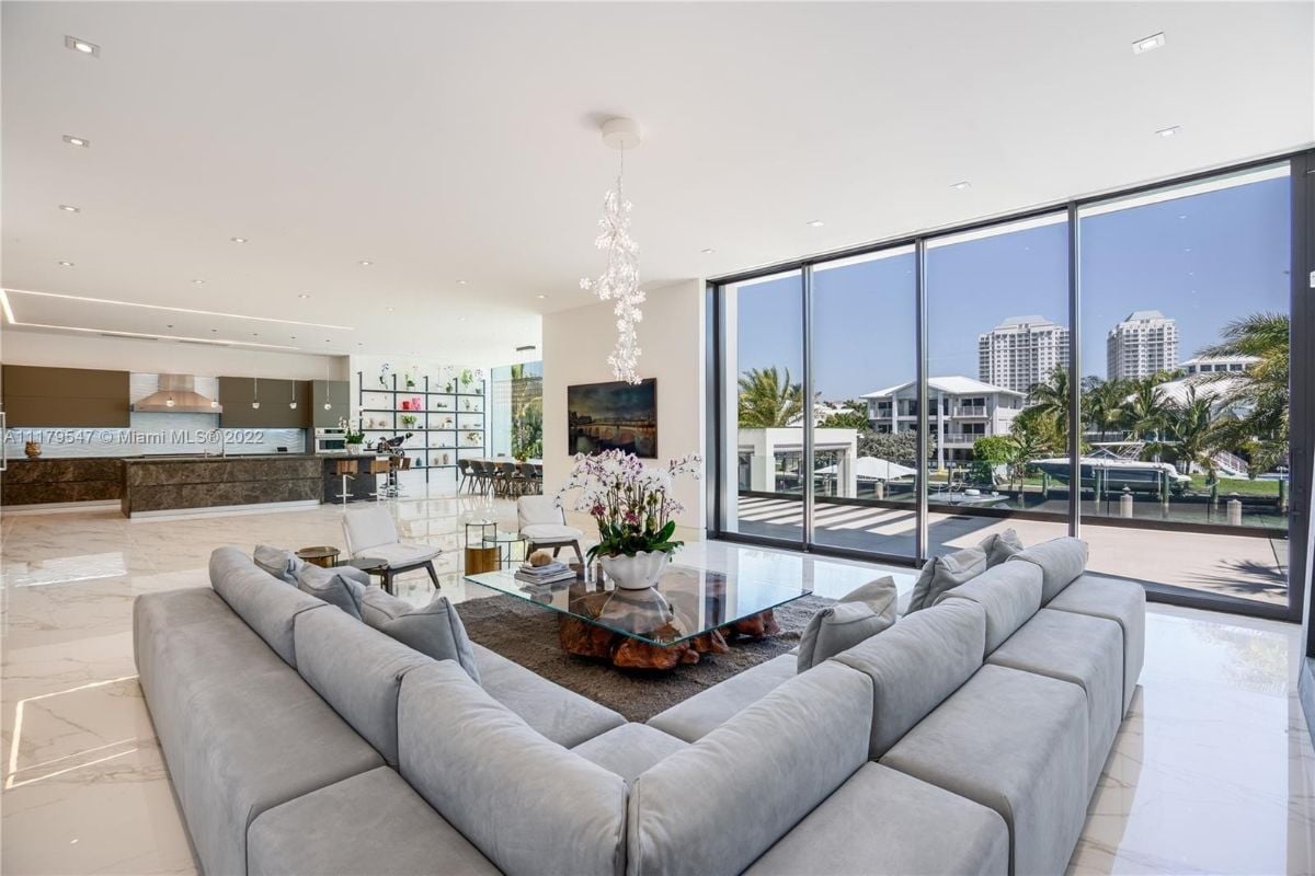 The living room features a sectional sofa, and the full-size glass windows showcase the ocean and the neighboring houses.