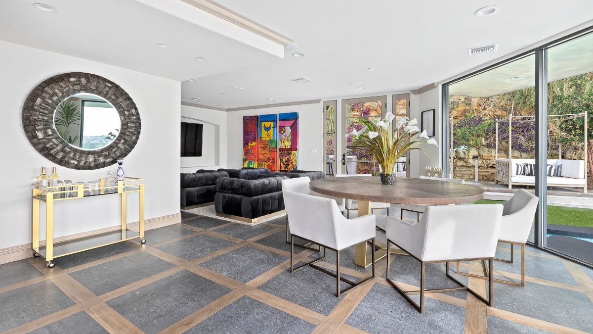 The square-shaped flooring and the wooden round table are also well-designed, and there are black sofas with a large television positioned to one side.