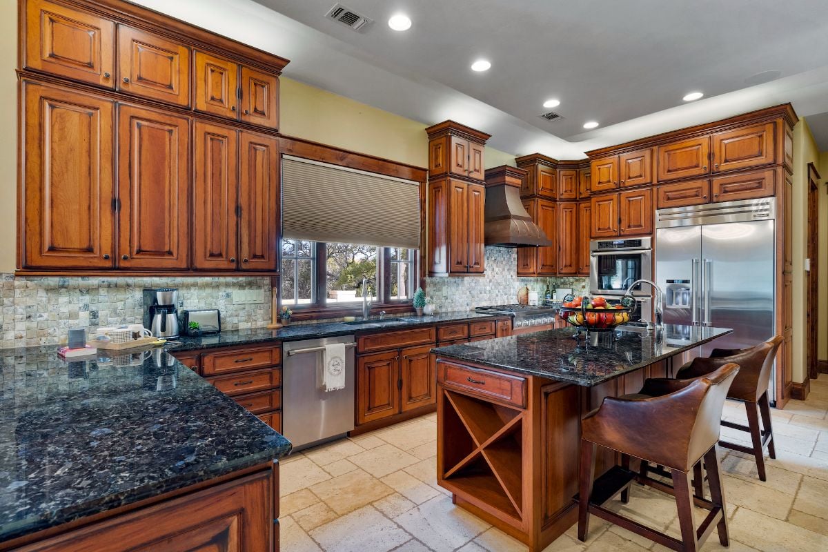 The kitchen features a bi-level kitchen island with a granite countertop that blends well with the wooden cabinet.