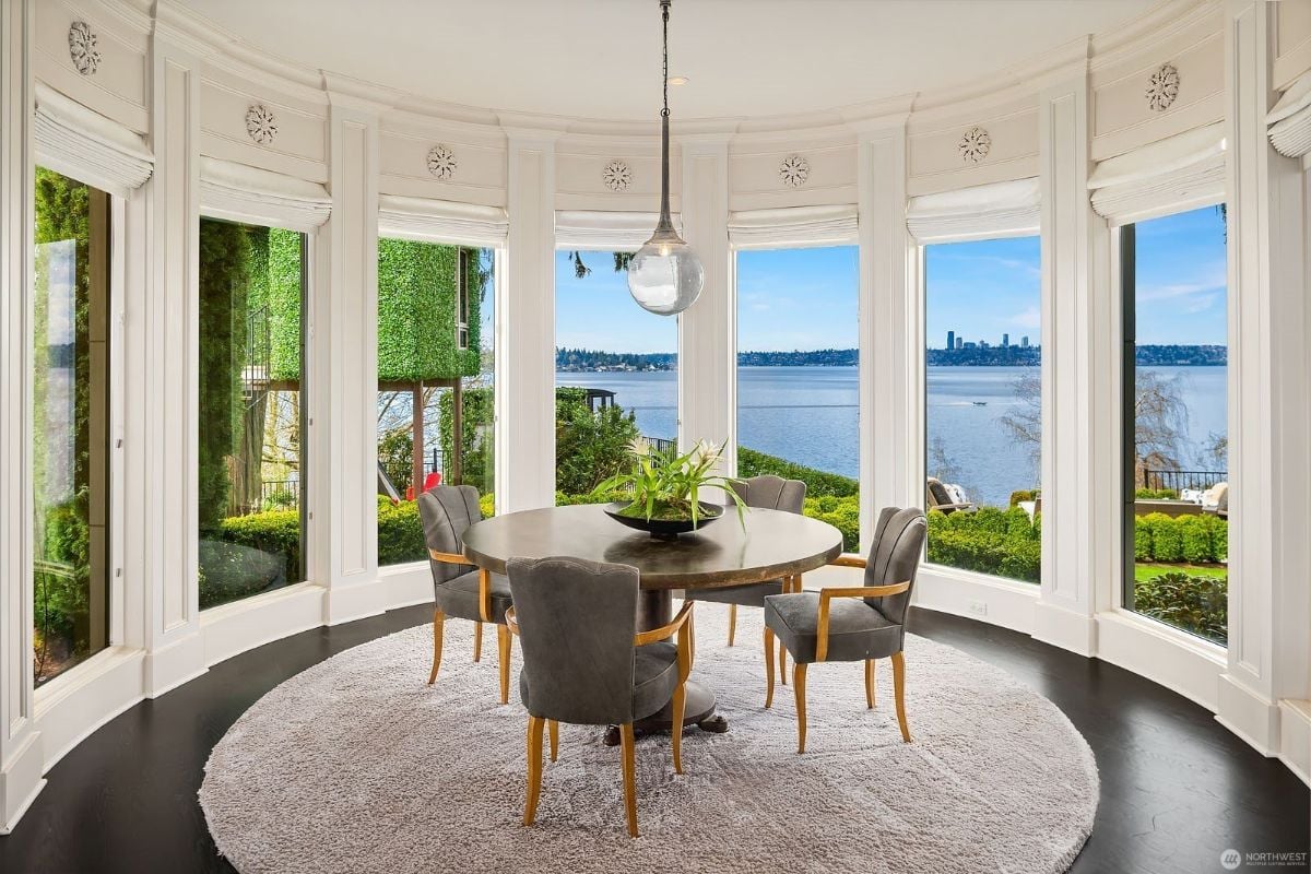 A dining room features a round table surrounded by glass walls showcasing the view of the sea.