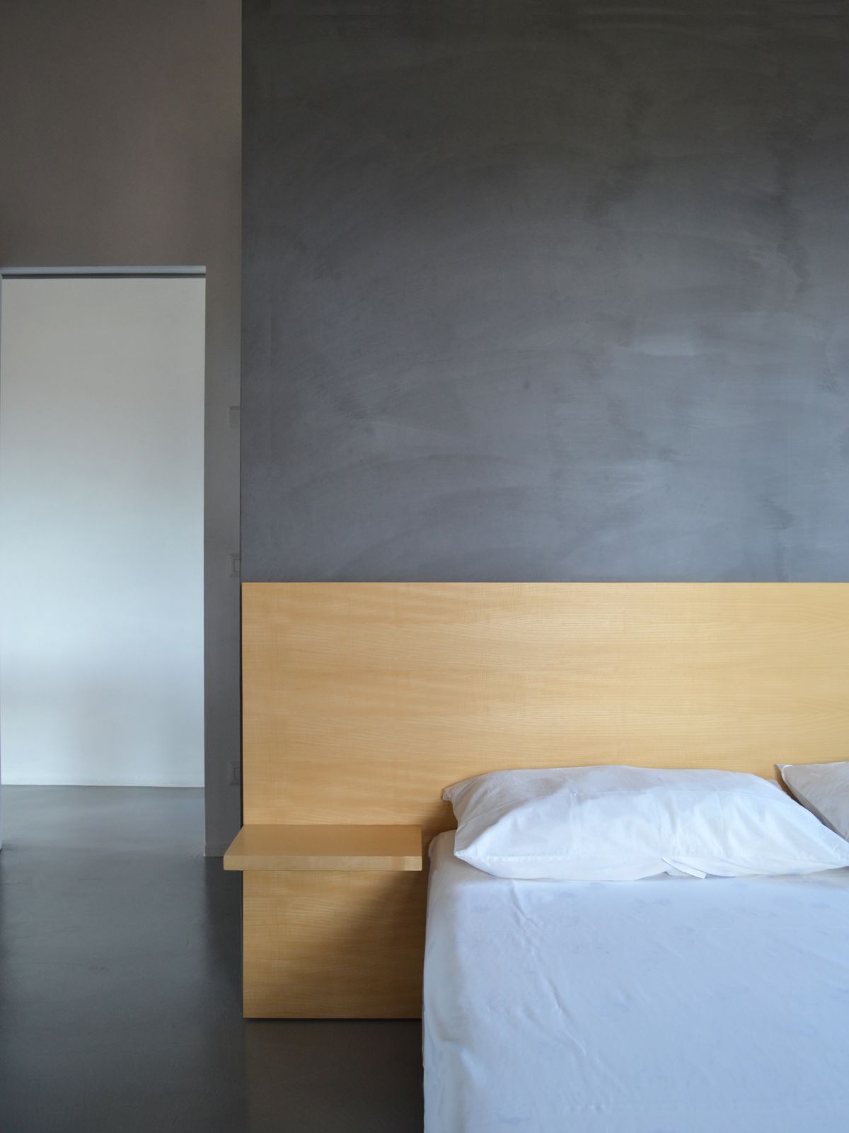 The bedroom features exposed concrete walls and a wooden headboard.