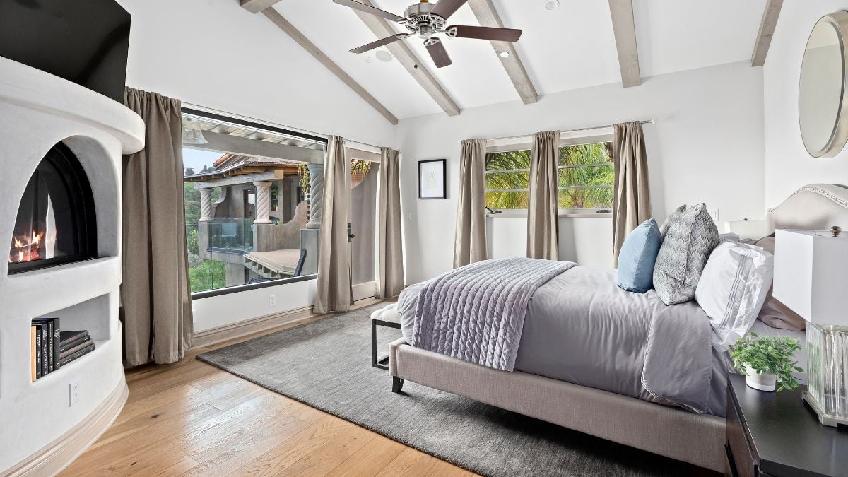 The bedroom has a wonderful view due of the large glass window, which also provides light throughout the space. The drapes and fireplace also give the area a charming appearance.