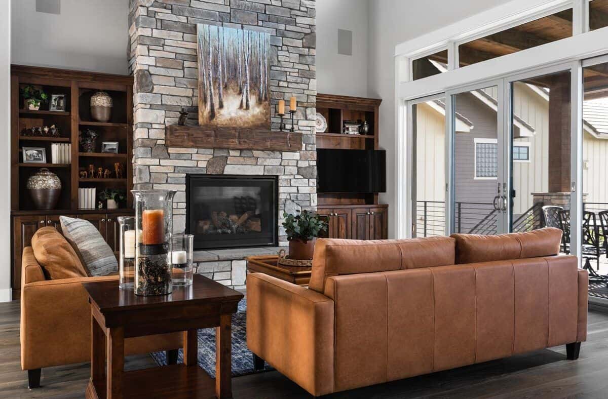The living room offers leather sofas and a brick fireplace flanked by dark wood built-ins.