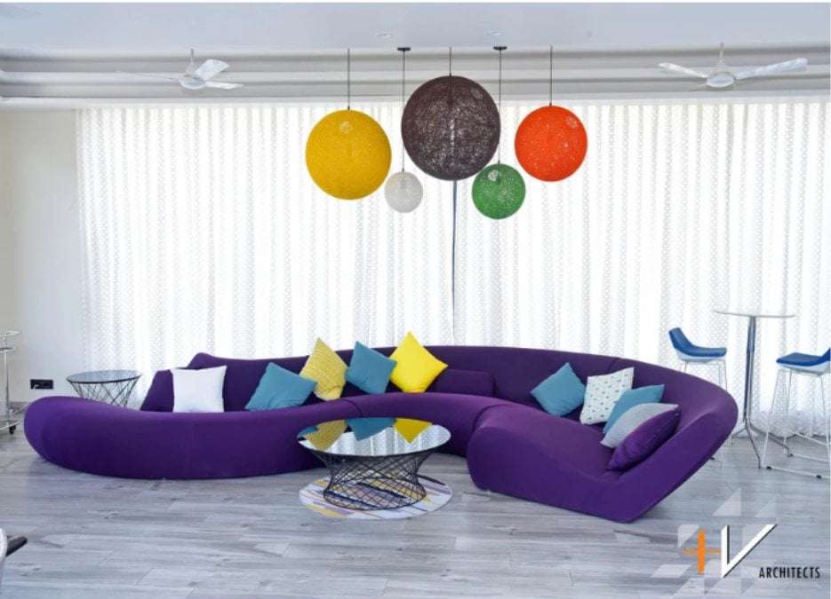 A violet S-shaped sofa with square pillows is placed in the center, while colorful and large circular lights can be noticed in the interior.