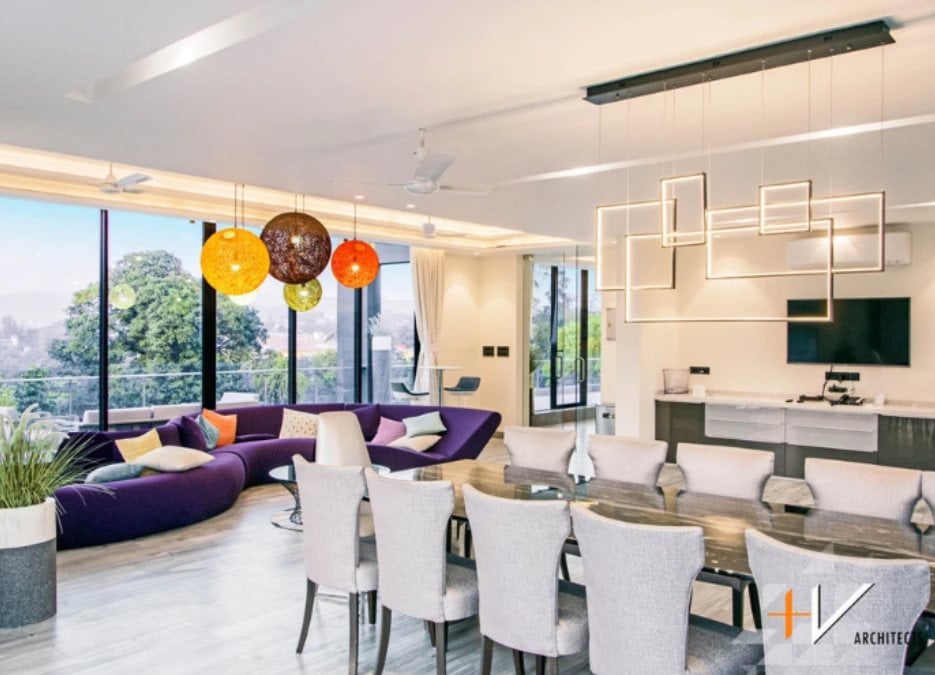 This is a shared photo of the kitchen and living section, where a dining table and a long S-shaped violet sofa are noticeable, along with a drop light in the kitchen.
