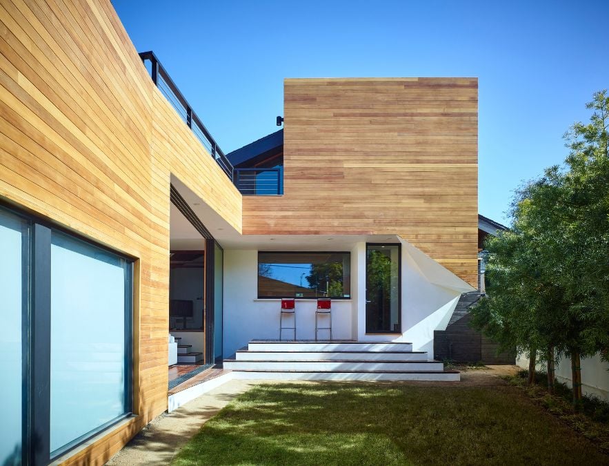 This description depicts a contemporary residence characterized by a wooden facade that lends it a sleek and modern appearance. A grassy courtyard further adds to the natural beauty of the property's surroundings.