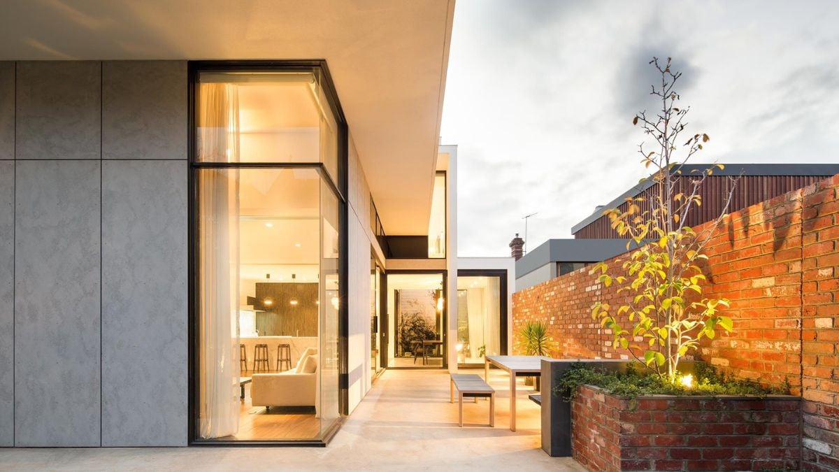 The modern house is characterized by a brick wall and expansive glass windows.
