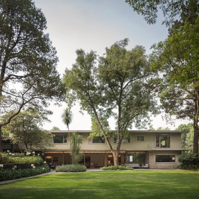 The house's exterior has been photographed during the daytime, displaying its intricate openwork structure, along with the spacious lawn and garden area with tall trees, providing a picturesque view of the property.