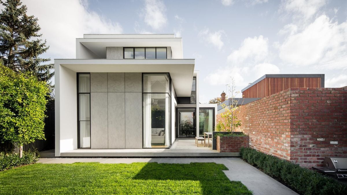 In the daytime, an exterior shot of the modern-designed Armadale House is captured, highlighting the brick wall fence and the verdant grass garden.