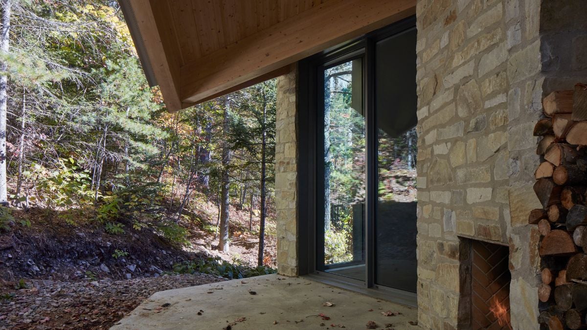 An outdoor stone fireplace is situated adjacent to a specific room and is complemented by a wooden ceiling featuring an overhanging design.