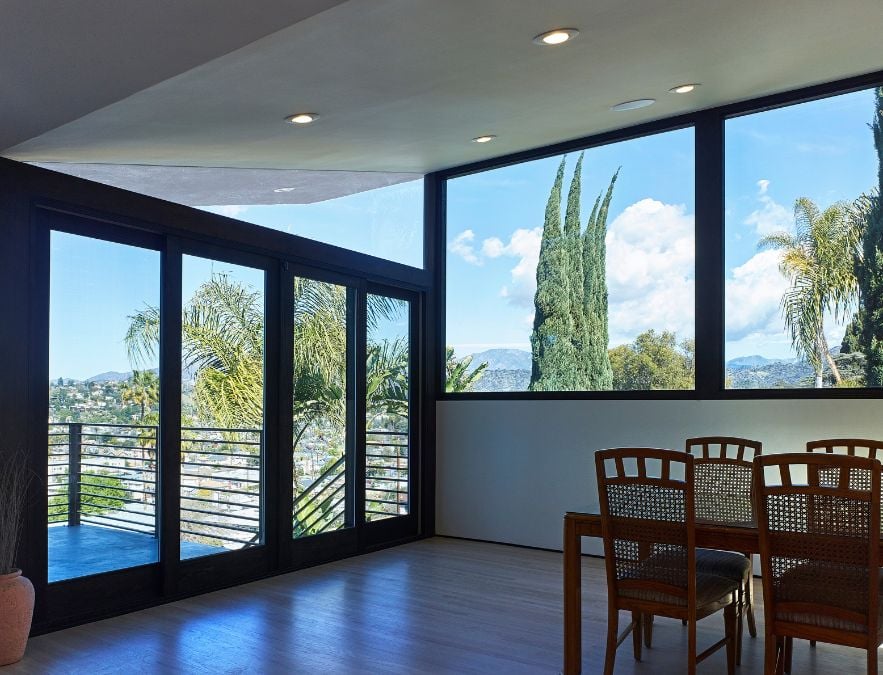 This setting features a dining table and accompanying chairs that offer a scenic view of the outdoor deck and its surroundings, which are visible through the glass doors and windows.