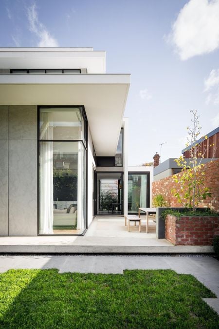 The exterior shot captures the outdoor area of the house, showcasing the brick wall and expansive glass windows.