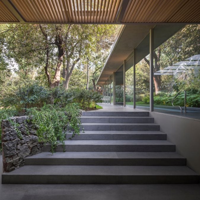 The photograph depicts a set of stairs that ascend towards the courtyard area, while simultaneously highlighting the vast expanse of glass walls that make up the house's structure.