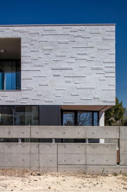 This close-up shot of the front facade showcases the marble-clad design and offers a glimpse of the veranda on the upper level.