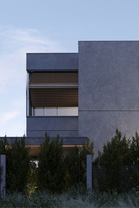 The exterior shot of the building, taken at dusk, showcases the foldable shutters on the windows and the lush green plants situated in front of the property.