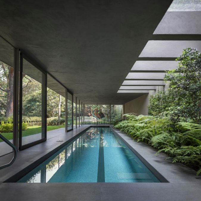 A focused shot that captures an enclosed, elongated swimming pool that boasts a set of skylights above it, also highlights the striking vegetation design present on the pool's side.
