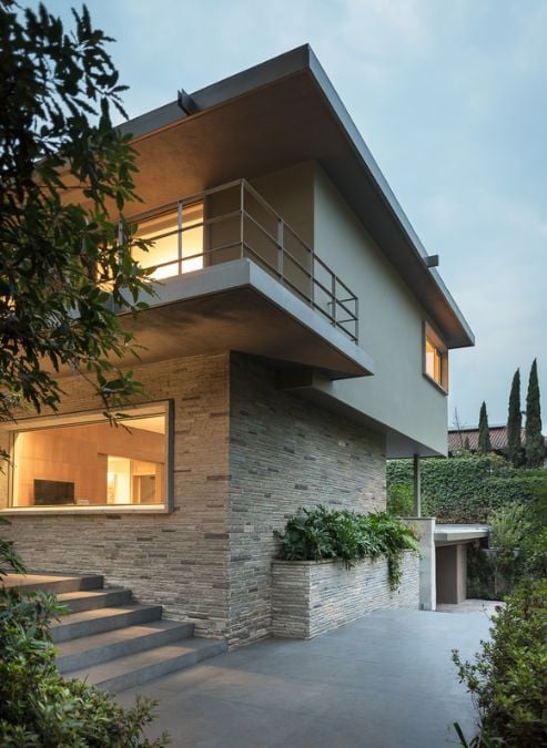 This contemporary house features a sleek staircase leading to the upper floor, serving as a stylish focal point in the space. The first floor is clad in modern wall cladding, while the second floor is finished with a smooth paint application,