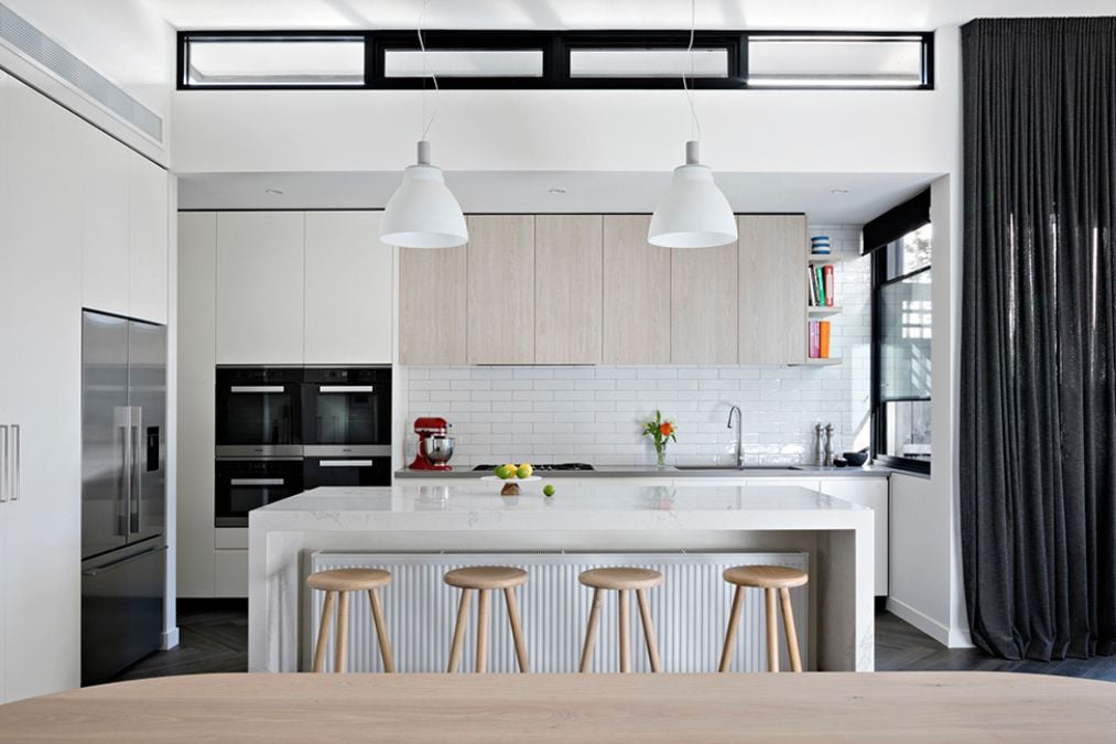 A modern kitchen with a white color scheme featuring a central island and two pendant lights.