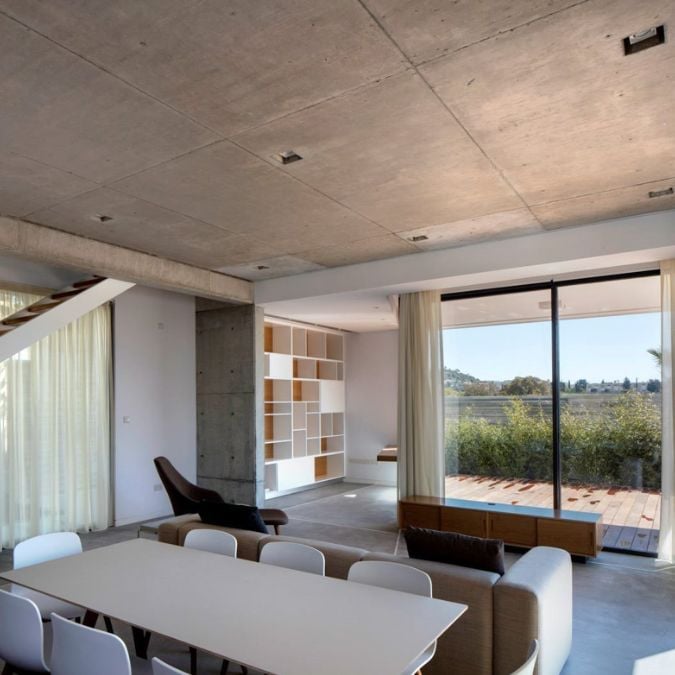 This interior shot of the living section highlights the beautiful view outside through huge glass panels, and features a layout with raw concrete that adds to the house's charm.