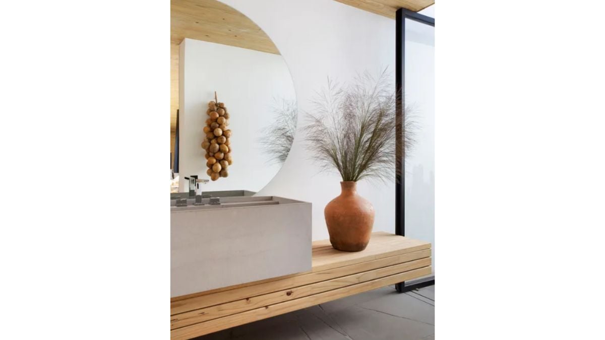 A big circle mirror on a sink and wooden furniture that supports it.