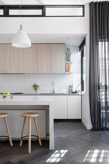 This is a portrait photograph that highlights the central island in a contemporary white kitchen area, with two pendant lights adding to the modern aesthetic.