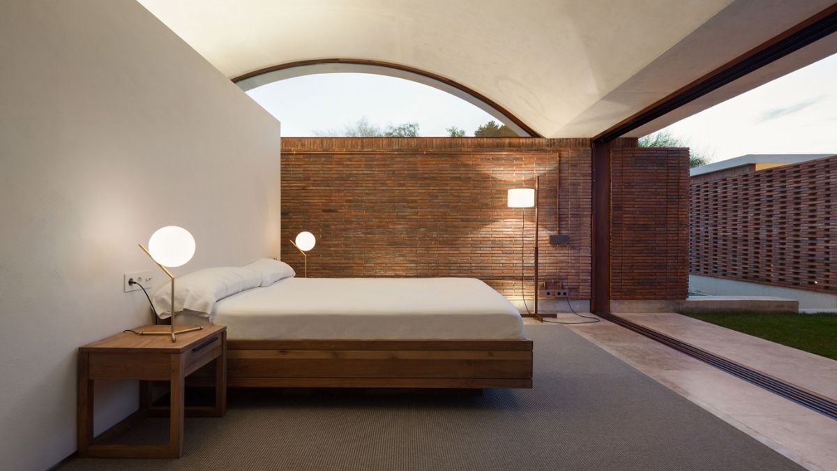 This spacious bedroom features an open wall adorned with several yellow LED lamps and lamp shades, adding a warm and cozy ambiance to the room while highlighting the wall's unique design.