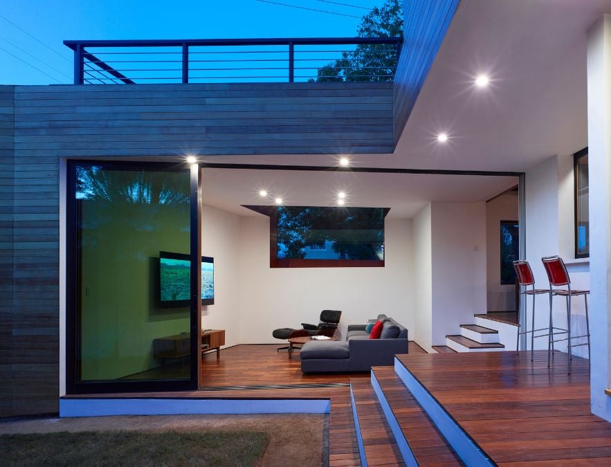 An exterior shot at nighttime, which portrays a living room and a glimpse of the roof deck railing, as seen from an external viewpoint.
