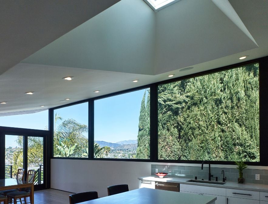 This photograph provides a close-up perspective of both the skylight and expansive glass windows, which offer a stunning view of the outdoors, with a focus on the towering trees.