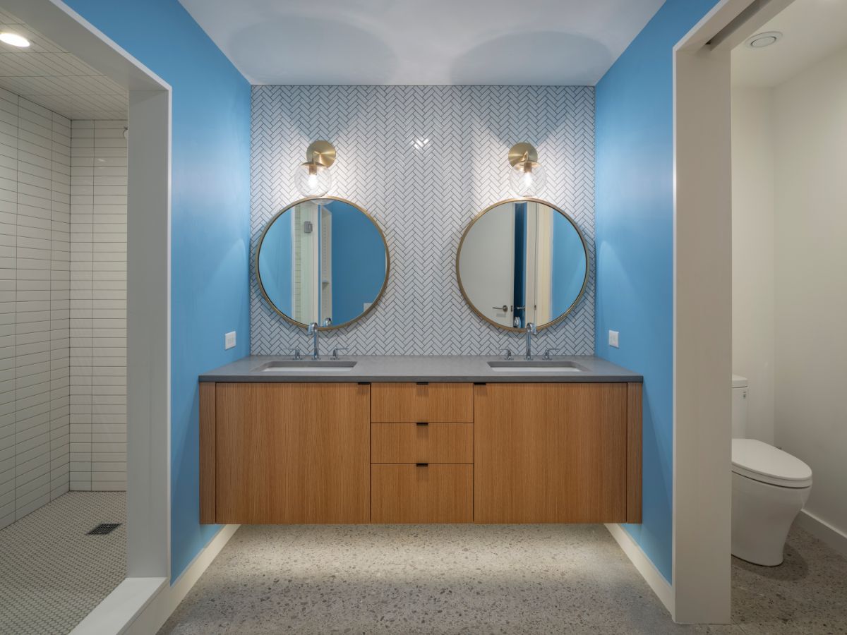 A bathroom with a vanity that functioned as the center of the toilet and shower area, with a fishbone pattern that contrasted with the light blue wall.