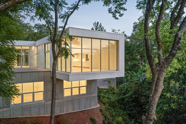 The house is grounded with a square exposed concrete foundation housing the “garden level” of bedrooms and office facing the wooded site toward the Plaza.