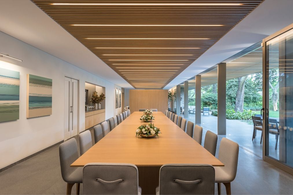 The image depicts a long dining table made of wood and accompanied by a set of elegant chairs.
