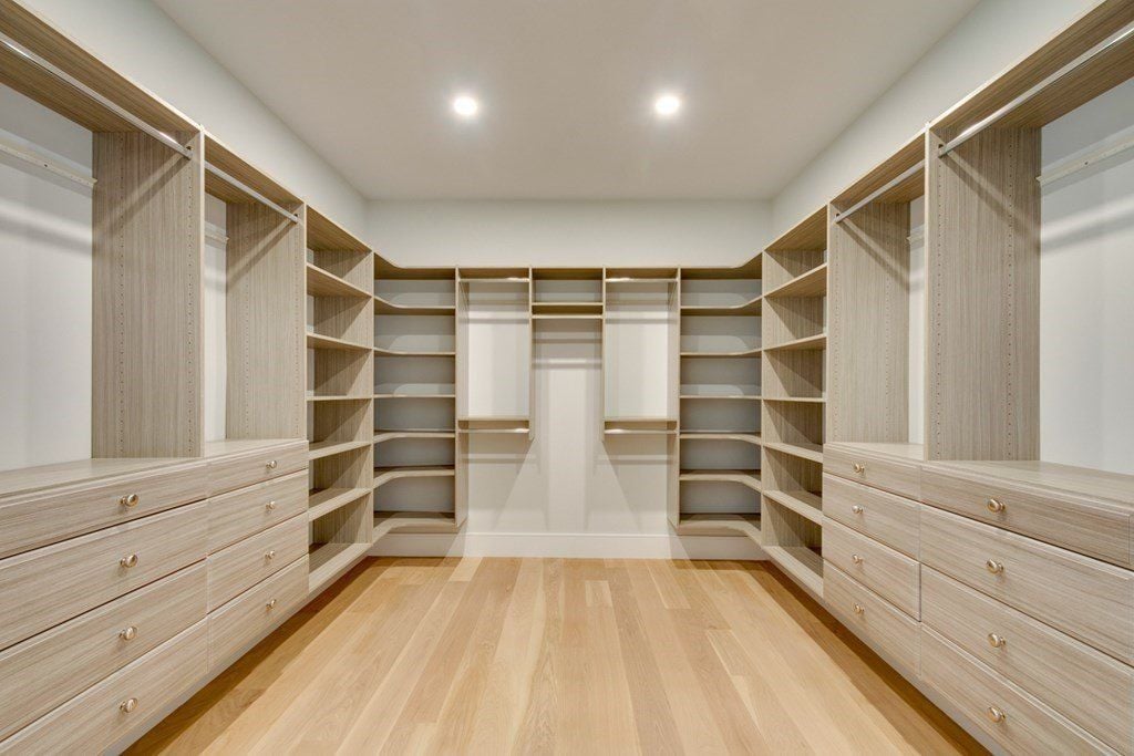 The walk-in closet features wooden flooring that goes well with the wooden shelves.