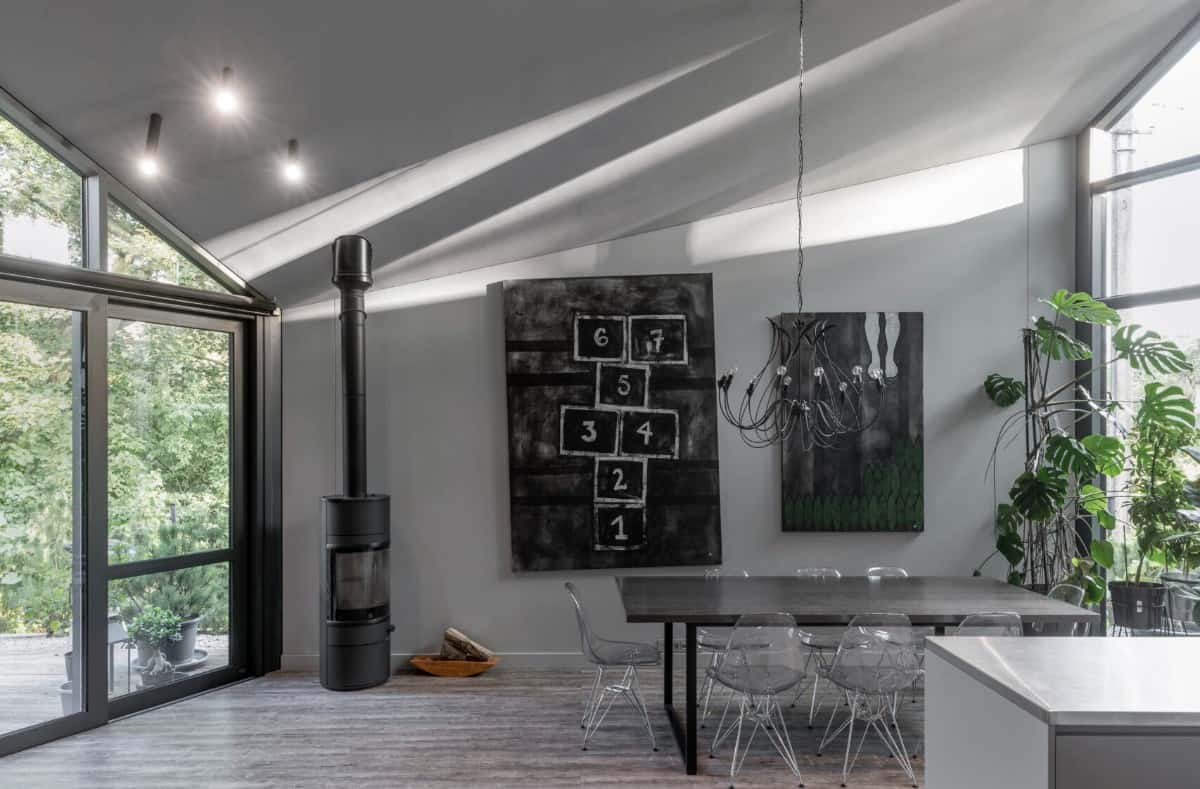 The dining area is decorated with dark artworks, a wood stove, and a wrought iron chandelier hanging over the contemporary dining set.