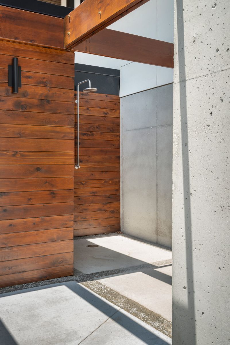 An open outdoor shower with white plaster walls and brown wood trim.