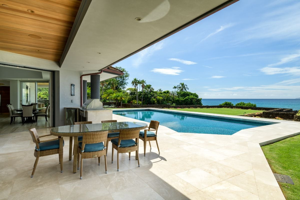 The outdoor dining features a rattan table with a glass top and an outdoor grill