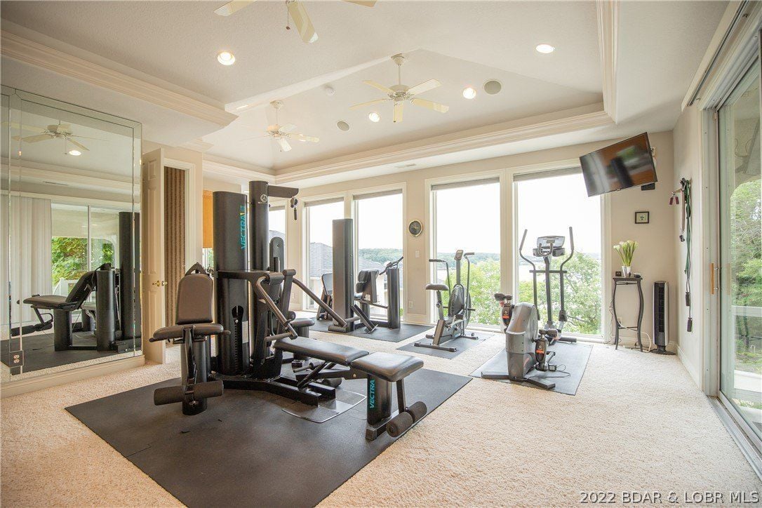 The home gym features a wall-to-wall carpet and glass walls that showcase the view outside while exercising.