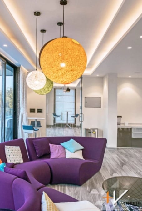 A violet S-shaped sofa with square pillows is placed in the center, while colorful and large circular lights can be noticed in the interior.