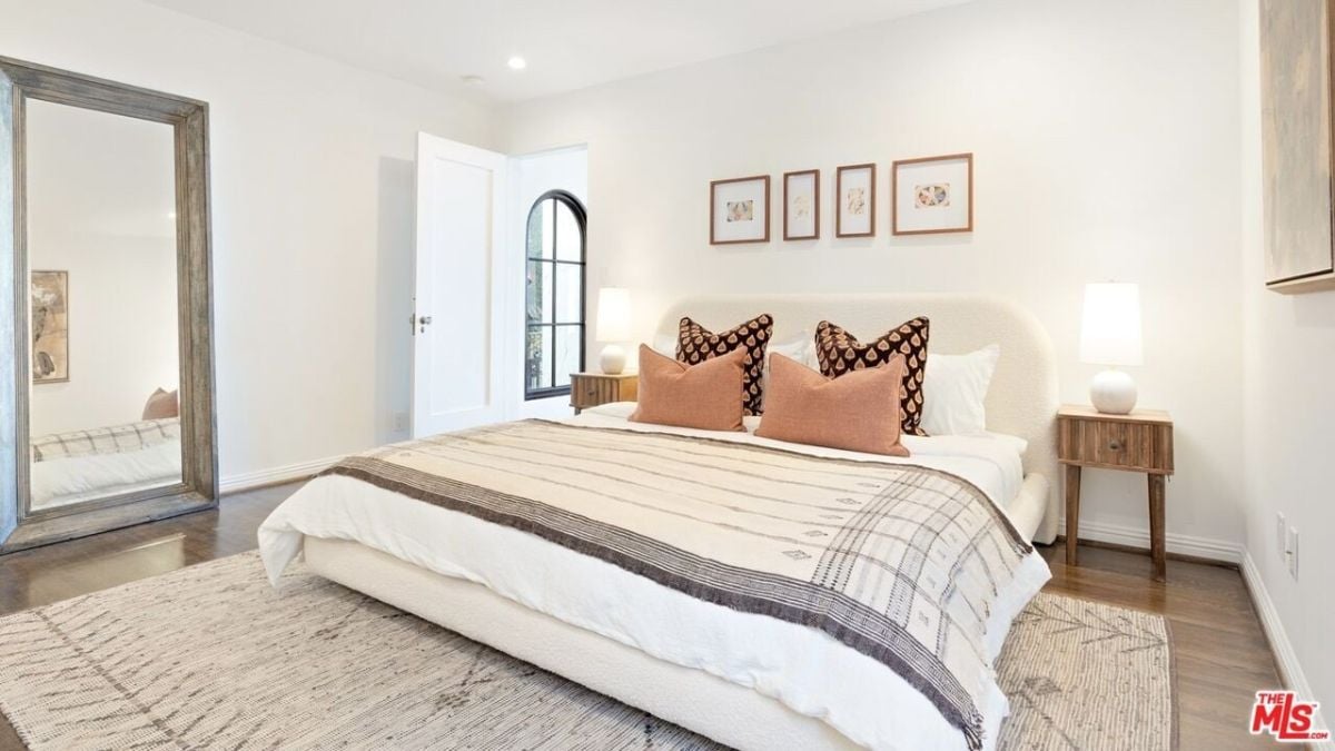 The en-suite room features a queen-sized bed and a classic framed full-length mirror that blends well with the lightly toned area rug.