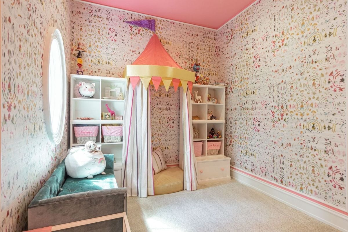 The kid's playroom features wallpaper and a wall-to-wall carpet that gives off a cozy feel.