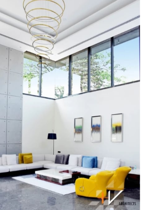 This is an interior shot of a high-ceiling living room filled with ring pendant lights, some wall art, and sofa corner set.