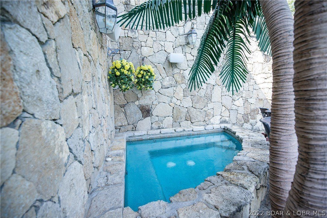 The outdoor spa is lit with wall lights, and the stone wall gives off a rough feel.
