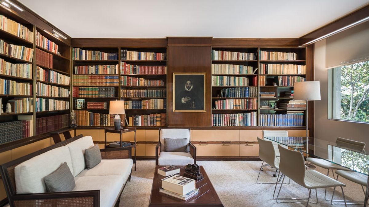 This captivating photo showcases a library room filled with an impressive collection of books and comfortable furniture, including chairs, tables, and reading lamps, creates a welcoming environment for reading and relaxation.