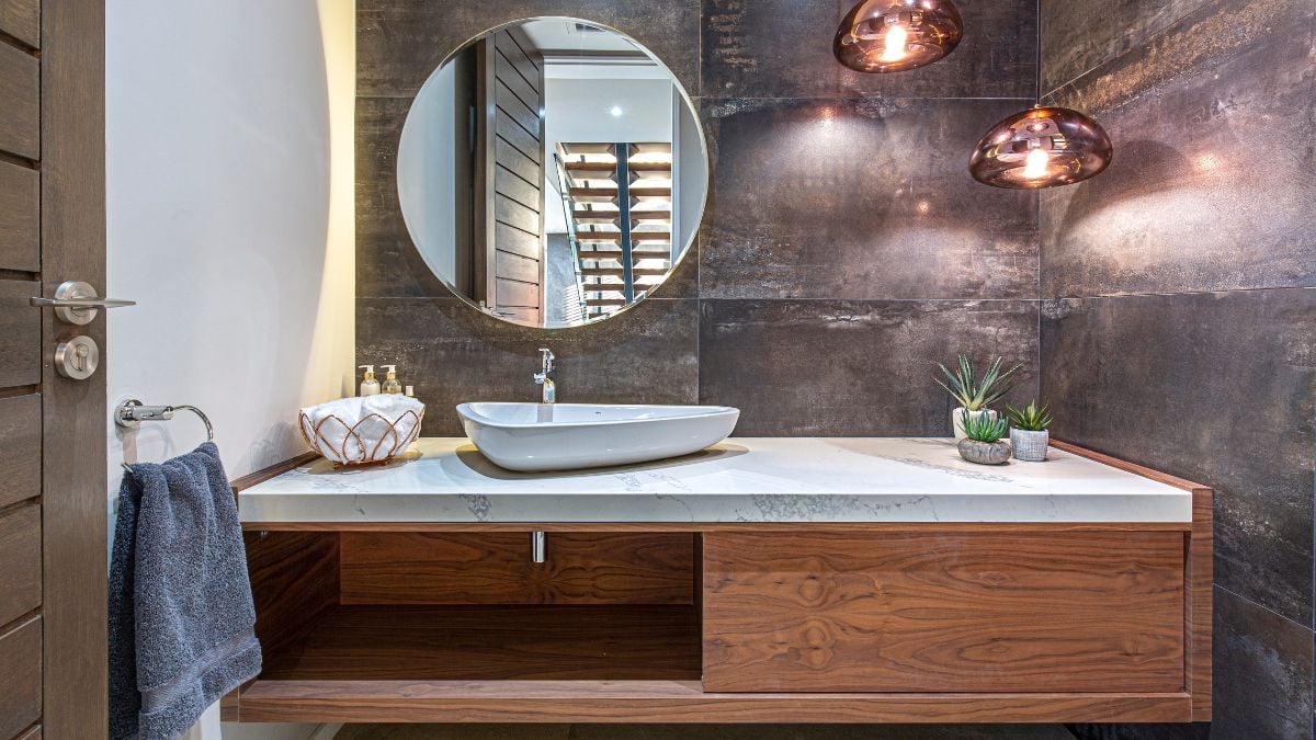 The wooden cabinets, round mirror, and grey walls of this sink's modest yet attractive design go nicely together.