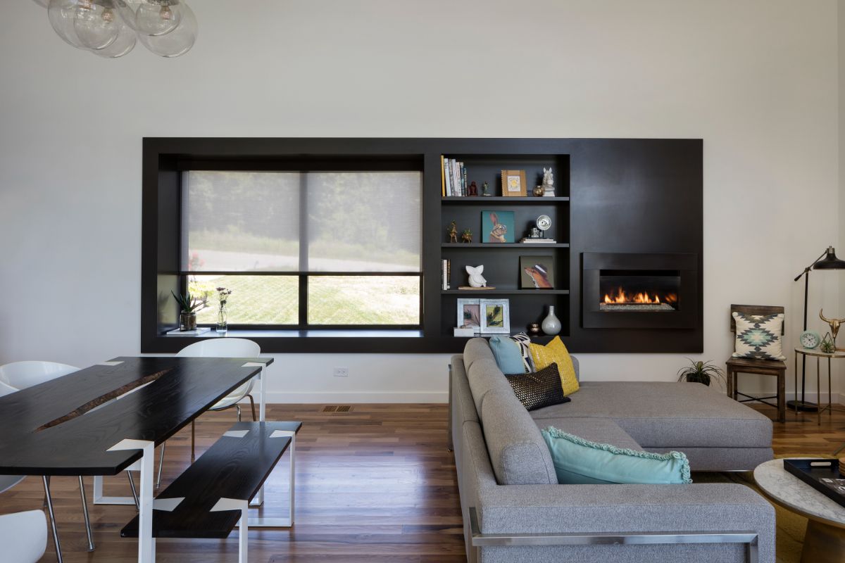 An open concept of dining and living area with a large window, open storage, and a fireplace built on dark paneling.