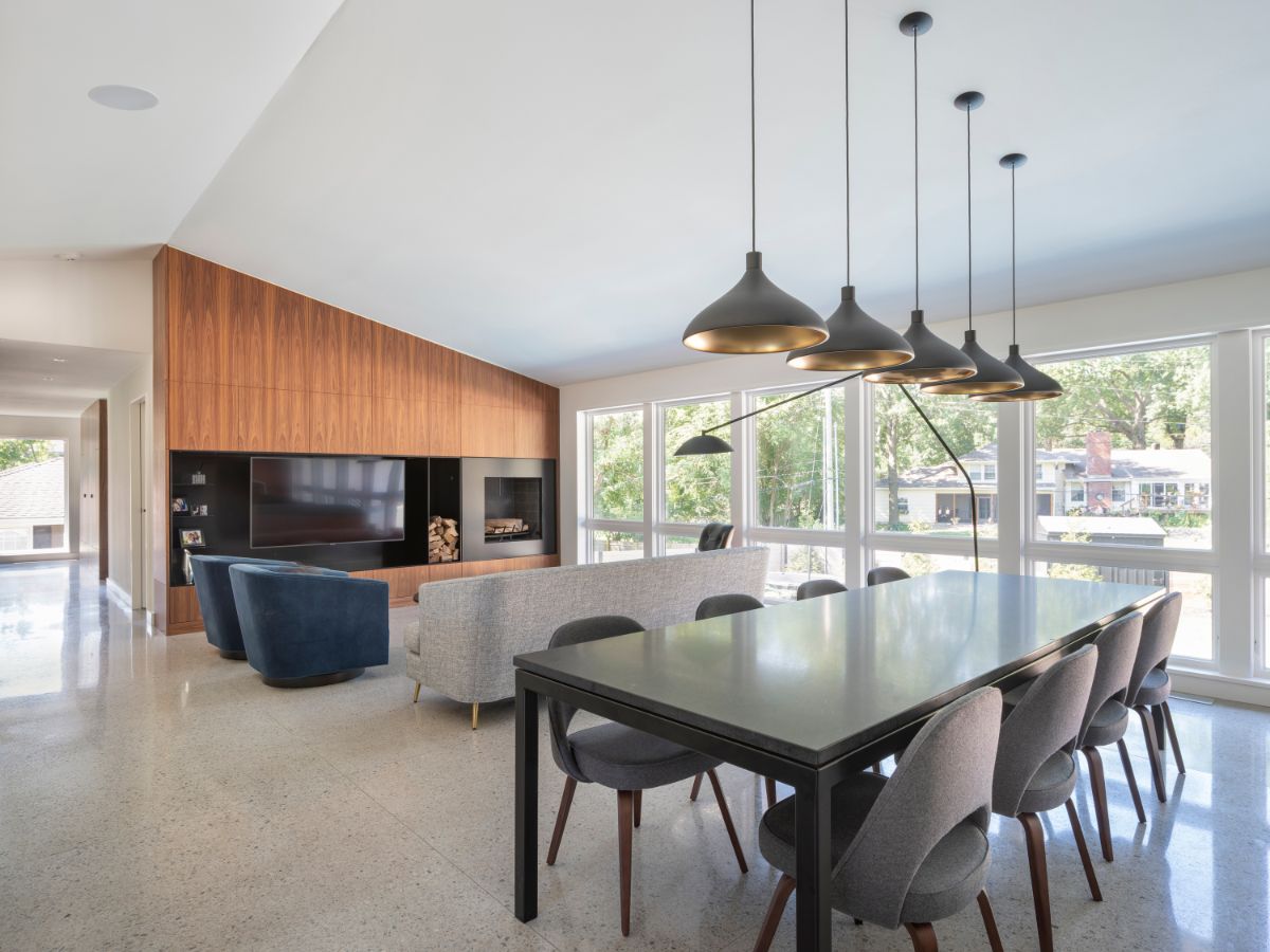 An open arrangement of the family room and dining area lighted by pendant lights suspended from the vaulted ceiling and natural light streaming in through the glass windows.