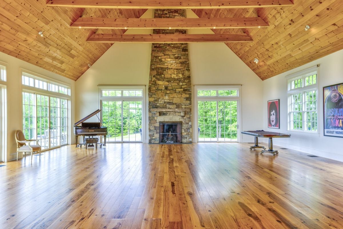 The large room with wooden flooring and ceiling features a fireplace and a piano.