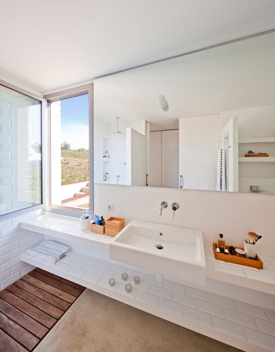A bathroom with floating shelves, a counter-topped sink, a wide mirror, and a view of sorrounding nature.