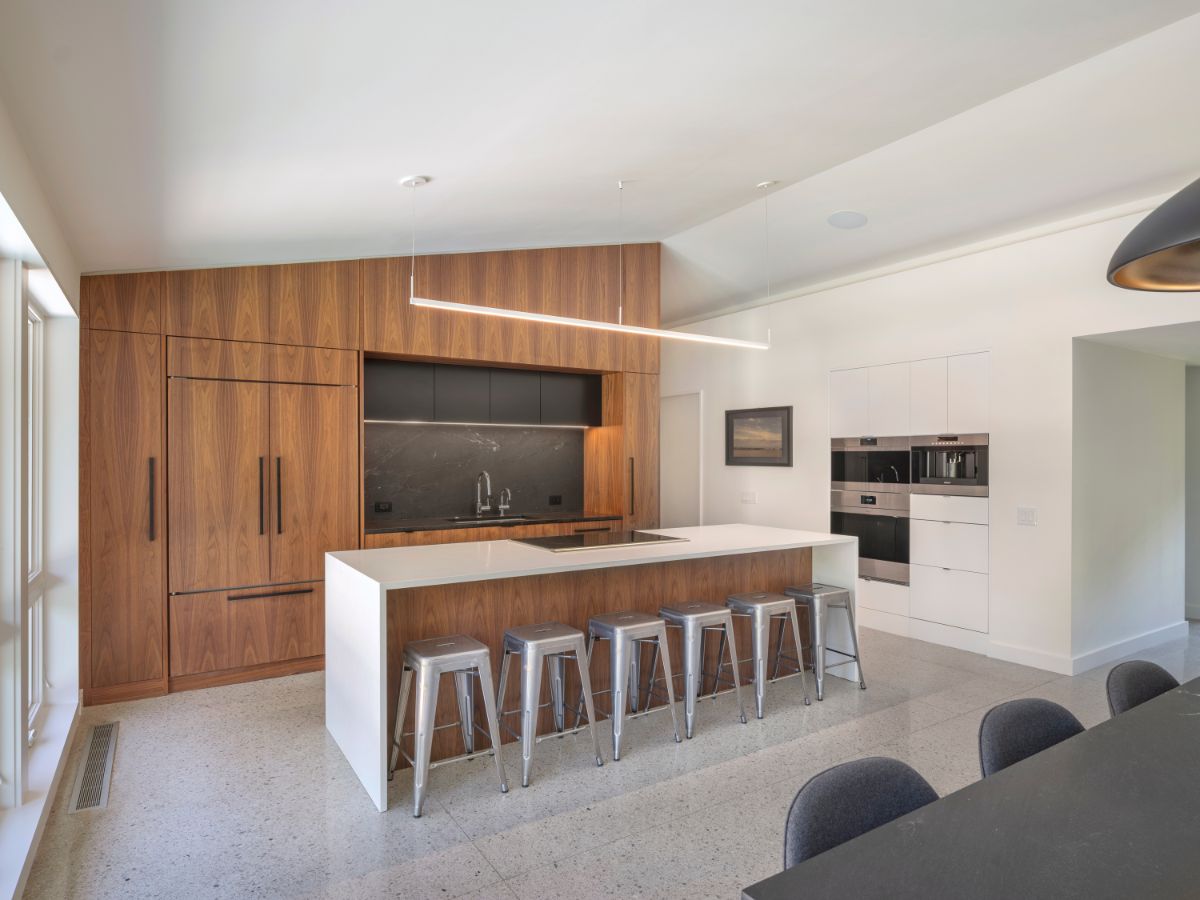 A kitchen with dark wood cabinet with a tile-topped island matched with metal bar stools and wall-mounted appliances.